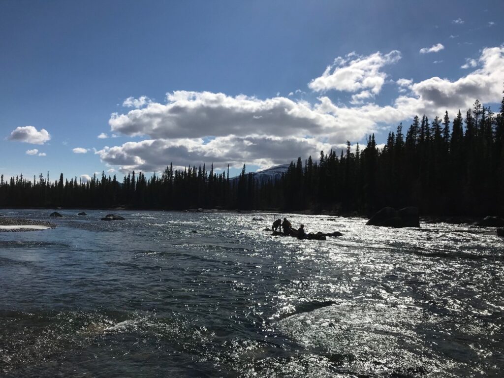 Canoe stranded in the middle of the river with the silhouette of people performing a rescue.